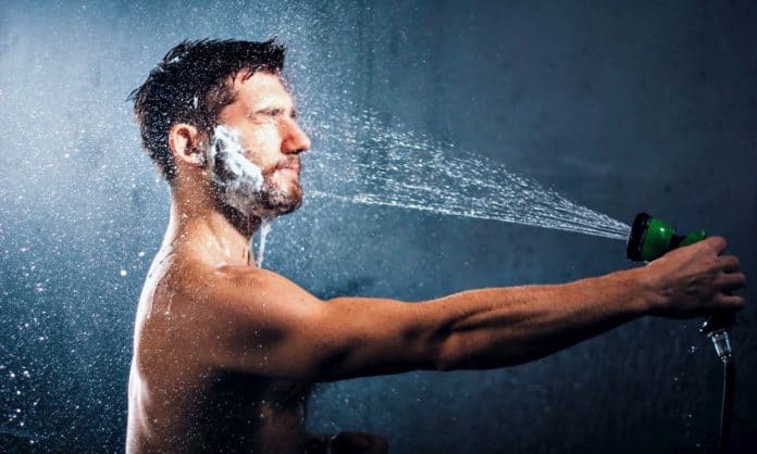 man washing his beard with a garden hose